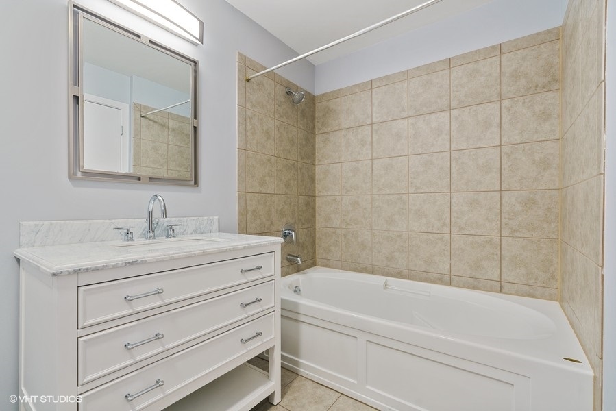 235 West Van Buren Street, Unit 4409 Chicago, IL 60607 - Photo 16 of 26 a bathroom with a granite countertop sink a mirror bathtub and shower