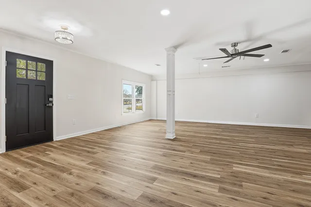 an empty room with wooden floor ceiling fan and windows