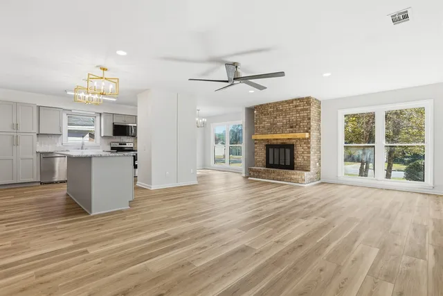 an empty room with wooden floor fireplace and kitchen view