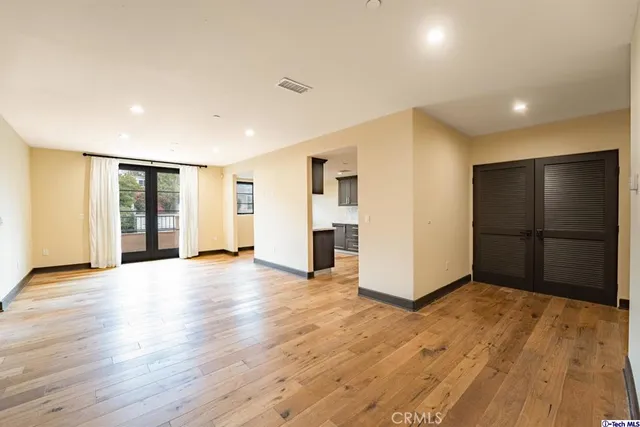 a view of an empty room with wooden floor and kitchen