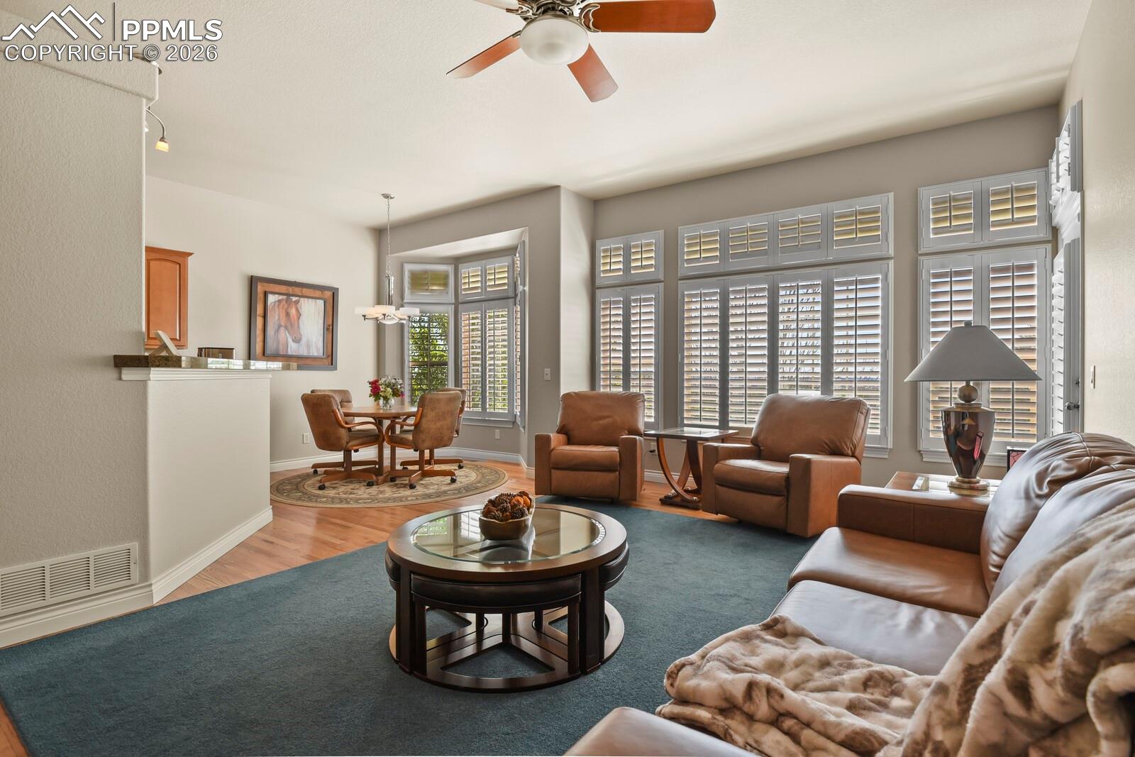 617 Concerto Drive Colorado Springs, CO 80906 - Photo 12 of 46 Bright living area featuring a ceiling fan, bay windows with plantations shutters, and hardwood flooring into the casual dining noom.
