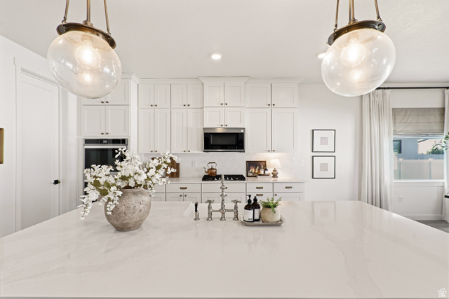870 North Ada Loop Lehi, UT 84048 - Photo 10 of 51 Spacious kitchen island featuring a light-toned countertop, dual pendant lighting, white shaker cabinetry, stainless steel appliances, and a tiled backsplash