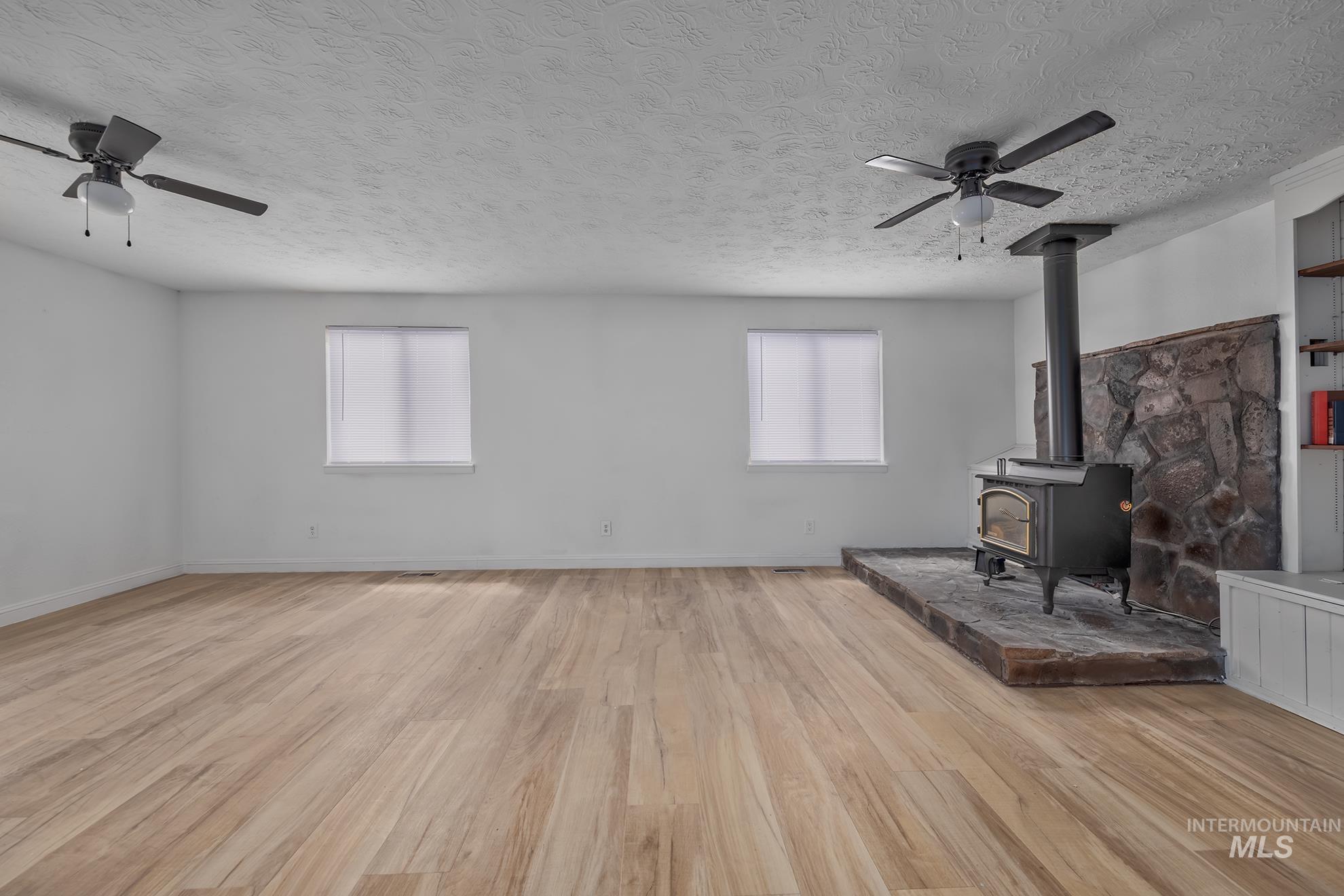 61 Southwest 4th Street Ontario, OR 97914 - Photo 17 of 42 Spacious interior featuring wood-finish flooring, a stone accent wall, and a free-standing wood stove with a dark pipe