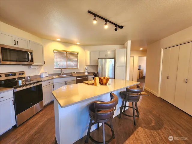 a kitchen with stainless steel appliances kitchen island granite countertop a table chairs sink and cabinets