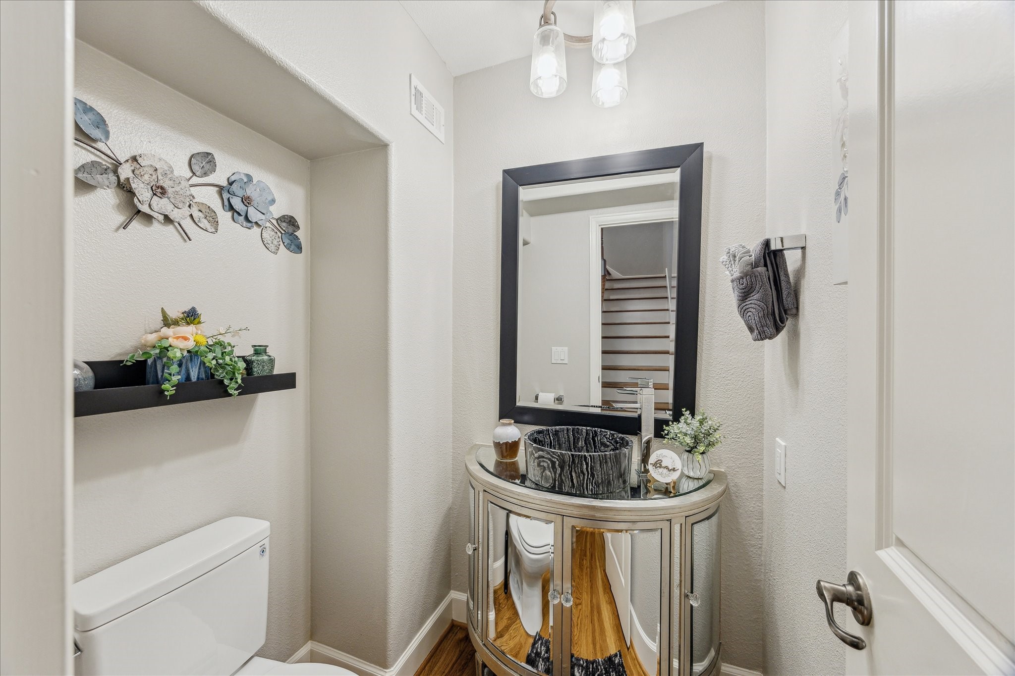 544 Bomar Street Houston, TX 77006 - Photo 28 of 43 GUEST POWDER ROOM... Accessed via a staircase landing with rich hardwood flooring, this stylish powder room features a custom mirrored vanity cabinet topped with a striking marble vessel sink. A framed mirror and decorative light fixture add elegance and charm, creating a refined space for guests.