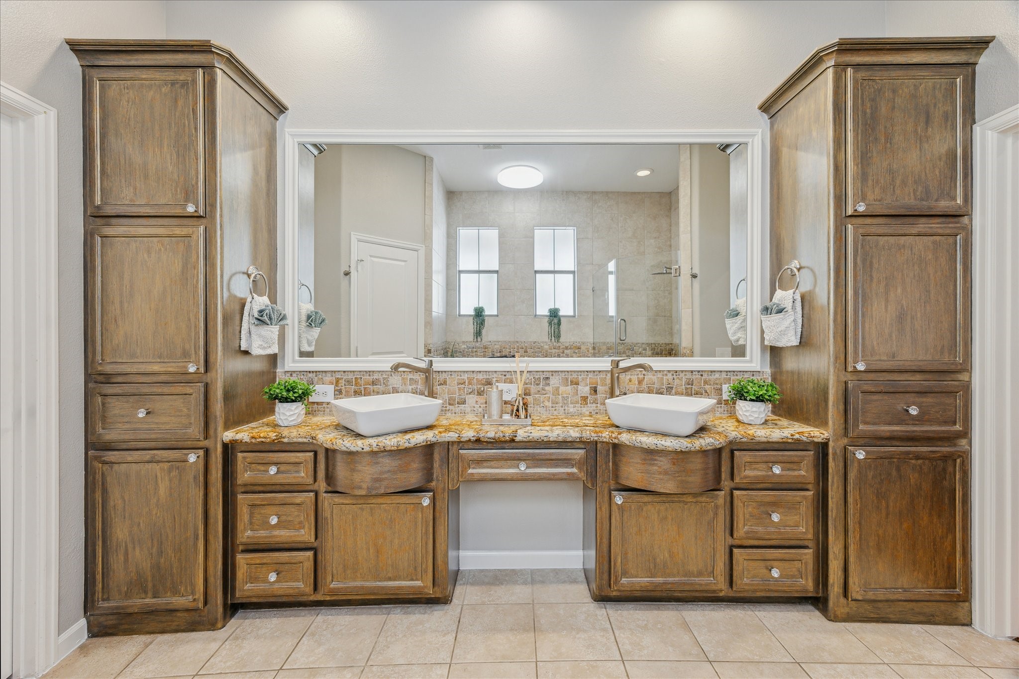 544 Bomar Street Houston, TX 77006 - Photo 33 of 43 PRIMARY BATH... This luxurious en suite bath features ceramic tile flooring and granite countertops with a refined bullnose edge. A travertine backsplash with decorative tile inlay adds a touch of elegance, while dual Ronbow ceramic vessel sinks sit atop a custom vanity with a framed mirror and separate makeup area. Ample custom built-ins provide exceptional storage, blending beauty and functionality in this serene retreat.
