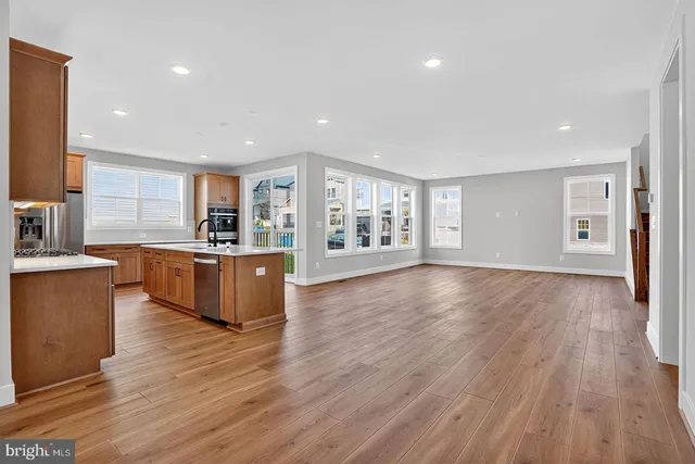 a large kitchen with stainless steel appliances granite countertop a large counter top a wooden floors and a large window