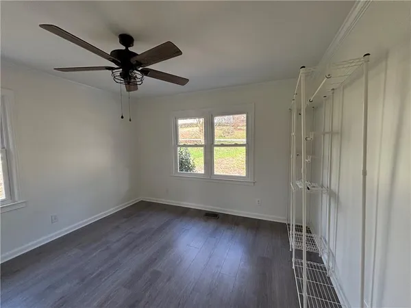 a view of a livingroom with a hardwood floor a ceiling fan and windows
