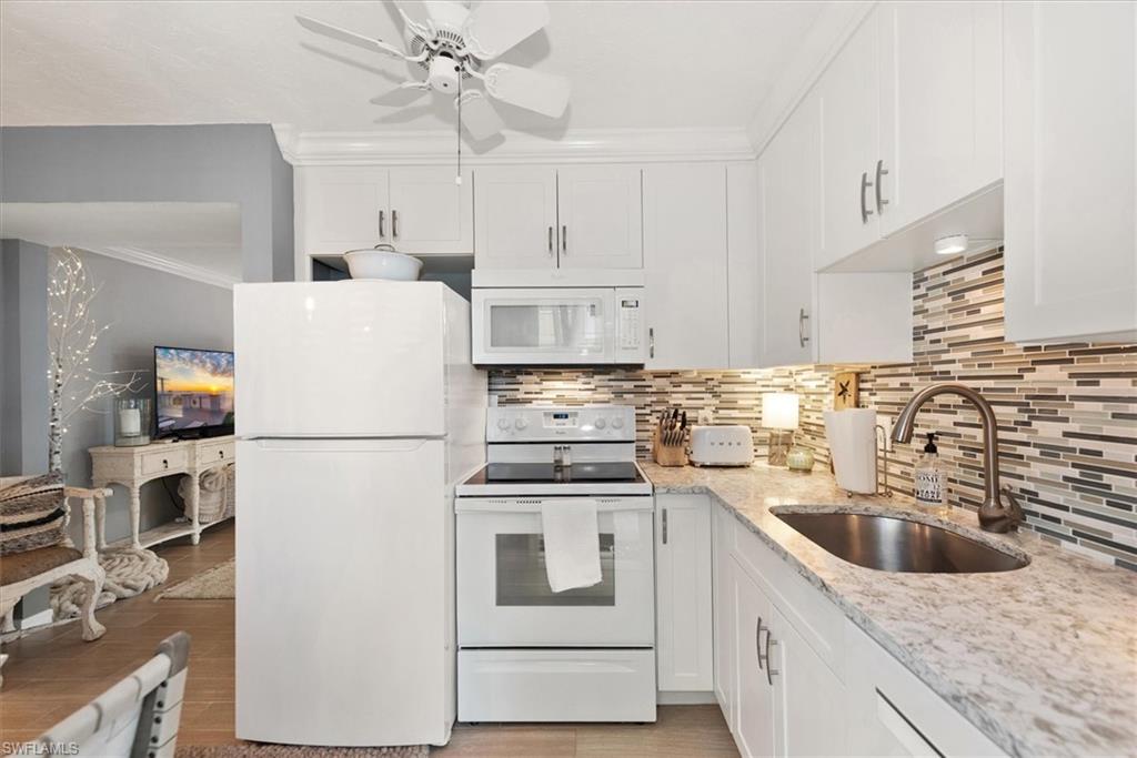 291A 8th Avenue South, Unit 291A Naples, FL 34102 - Photo 12 of 25 Kitchen with white appliances, white cabinetry, crown molding, light stone counters, and backsplash