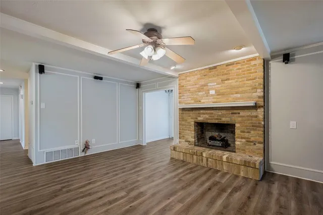 a view of a livingroom with a fireplace a ceiling fan and wooden floor