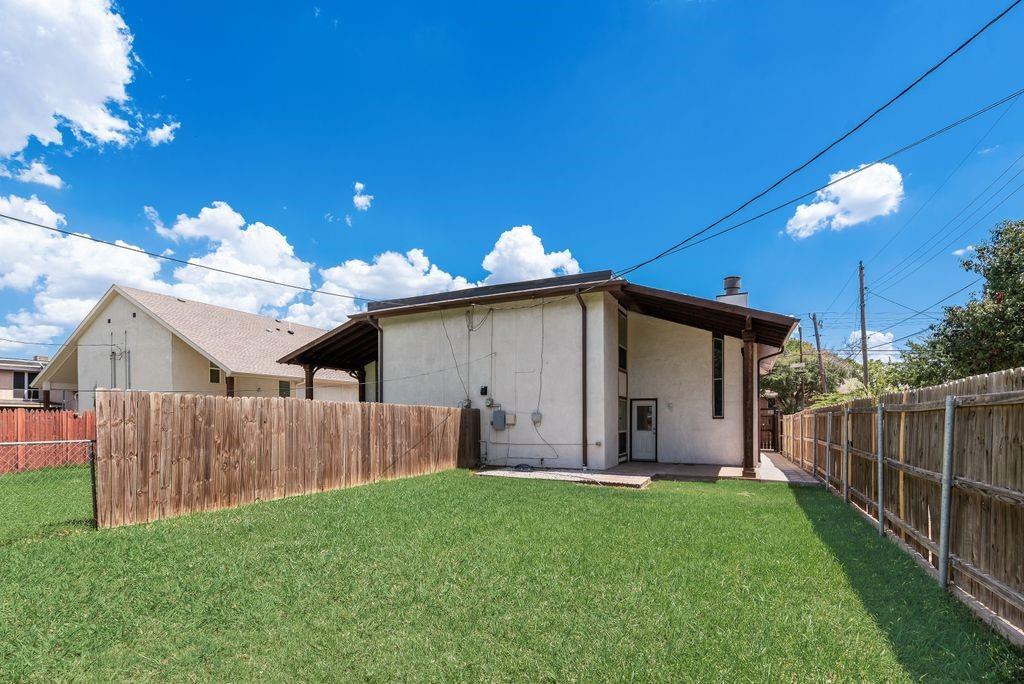 219 West Rochelle Road Irving, TX 75062 - Photo 29 of 29 Expansive backyard featuring a manicured lawn, a wood plank fence, and a covered patio area with a concrete slab