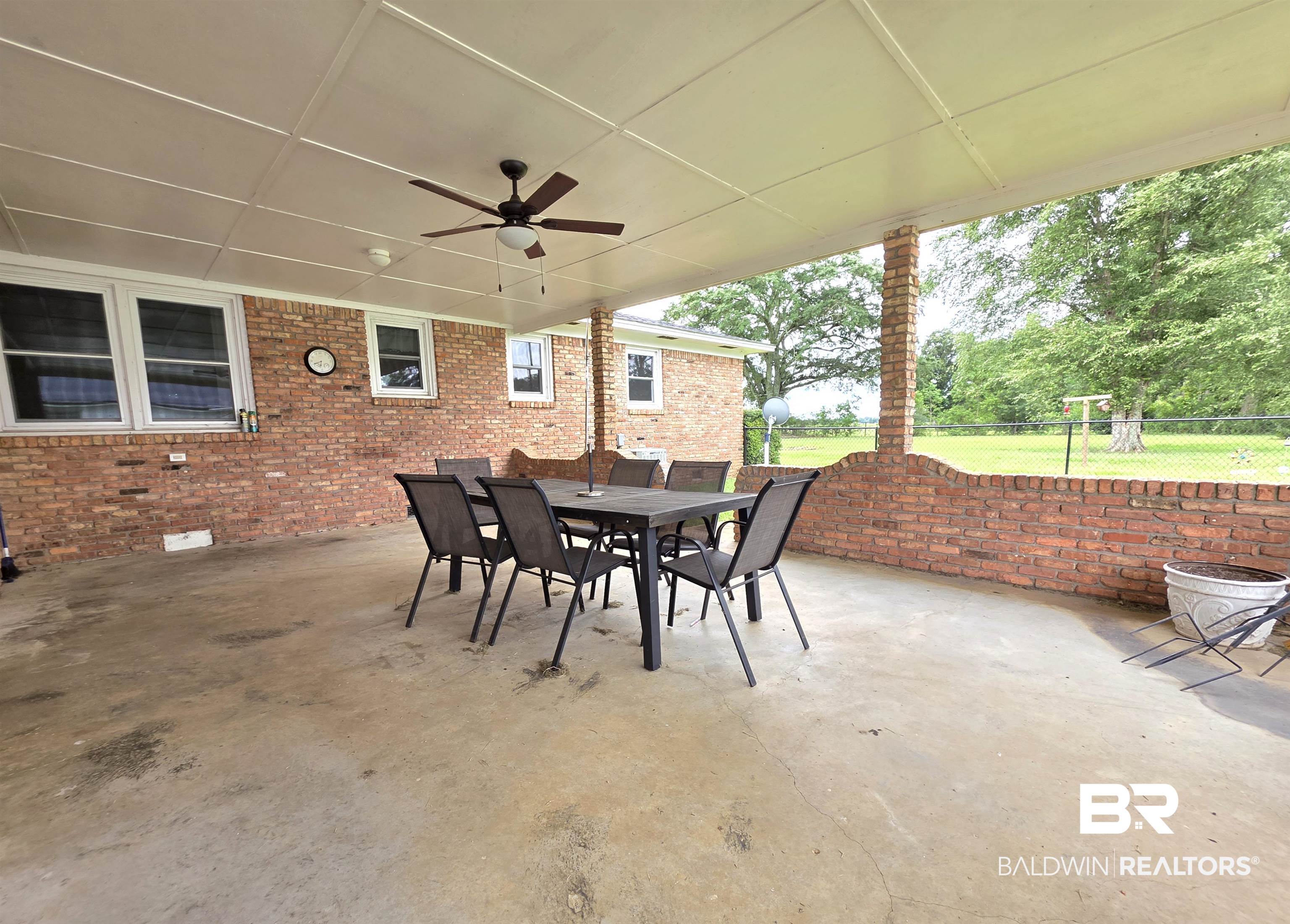 558 Stanton Road Atmore, AL 36502 - Photo 19 of 29 Expansive covered patio featuring a ceiling fan, brick half-wall, concrete flooring, and views of the surrounding green space