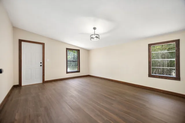 a view of an empty room with wooden floor and a window