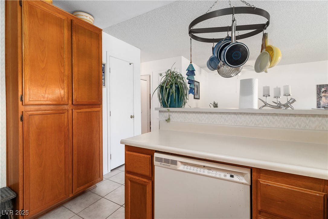2192 Aspen Mirror Way, Unit 102 Laughlin, NV 89029 - Photo 19 of 58 Kitchen featuring brown cabinets, dishwasher, light countertops, light tile patterned floors, and a textured ceiling