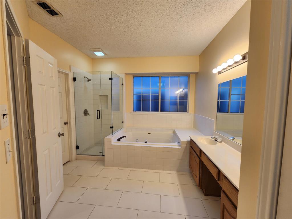 2413 Timber Ridge Lane Flower Mound, TX 75028 - Photo 15 of 32 Bathroom featuring a glass-enclosed shower, built-in bathtub, a double vanity with ample counter space, and a grid-pattern window