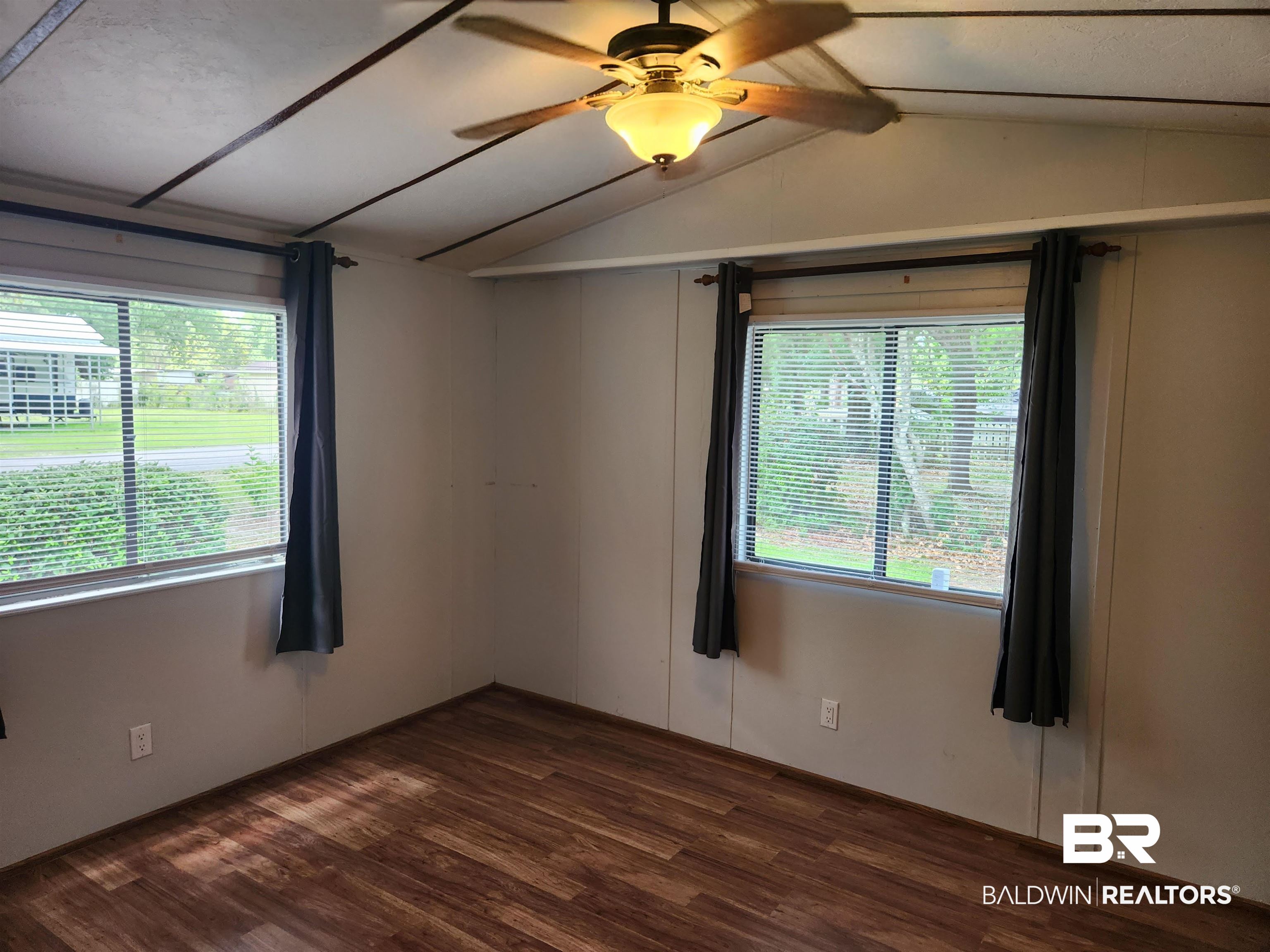 23051 Fritz Lane Foley, AL 36535 - Photo 25 of 26 Interior space featuring wood-finish flooring, two large windows with blinds, a ceiling fan with integrated lighting, and neutral wall paneling