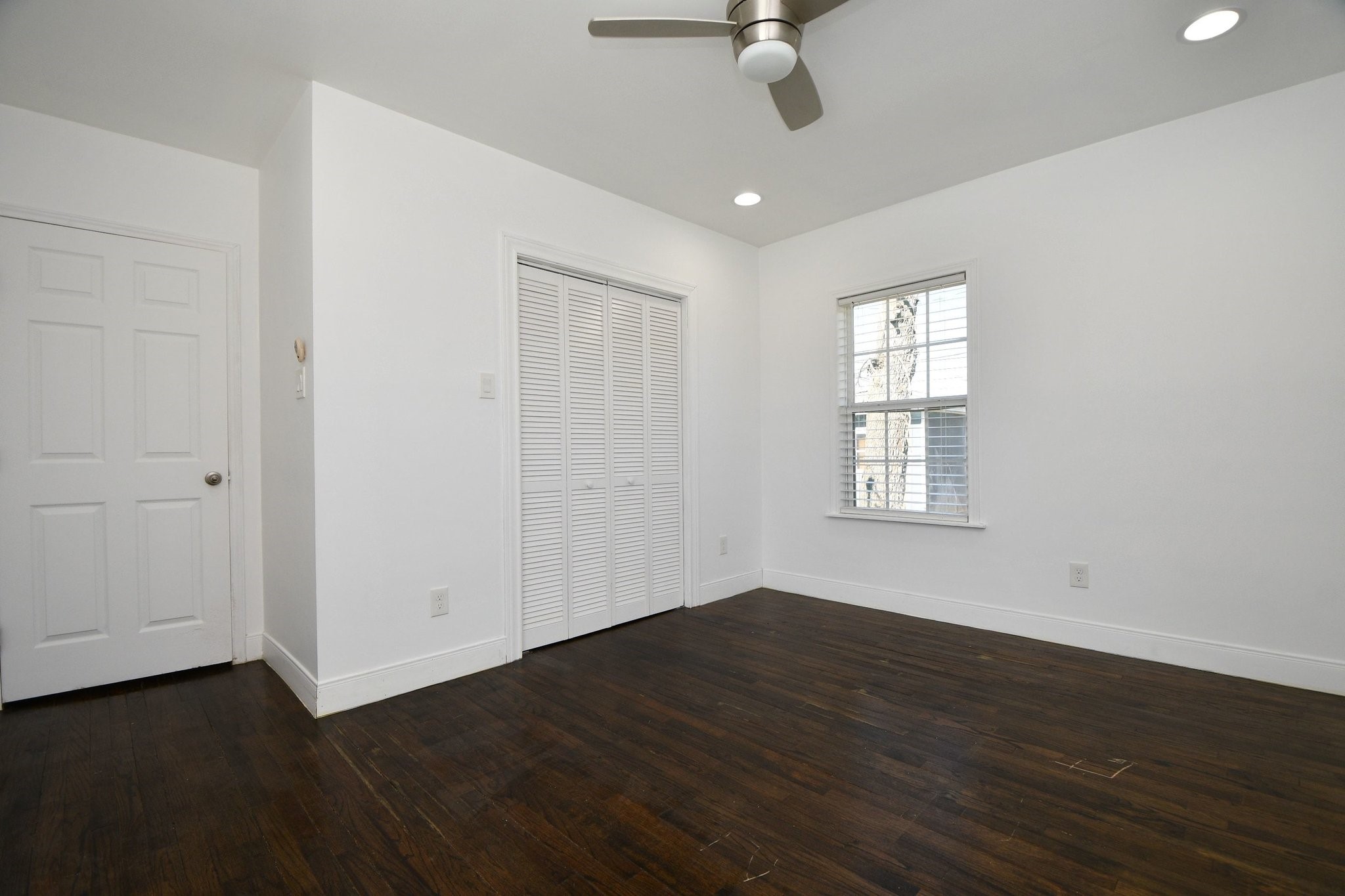 3803 Arbor Street Houston, TX 77004 - Photo 11 of 19 Bright, minimalistic room with hardwood floors, a ceiling fan, and ample natural light from the window. Features a closet with sliding doors and a simple white door.