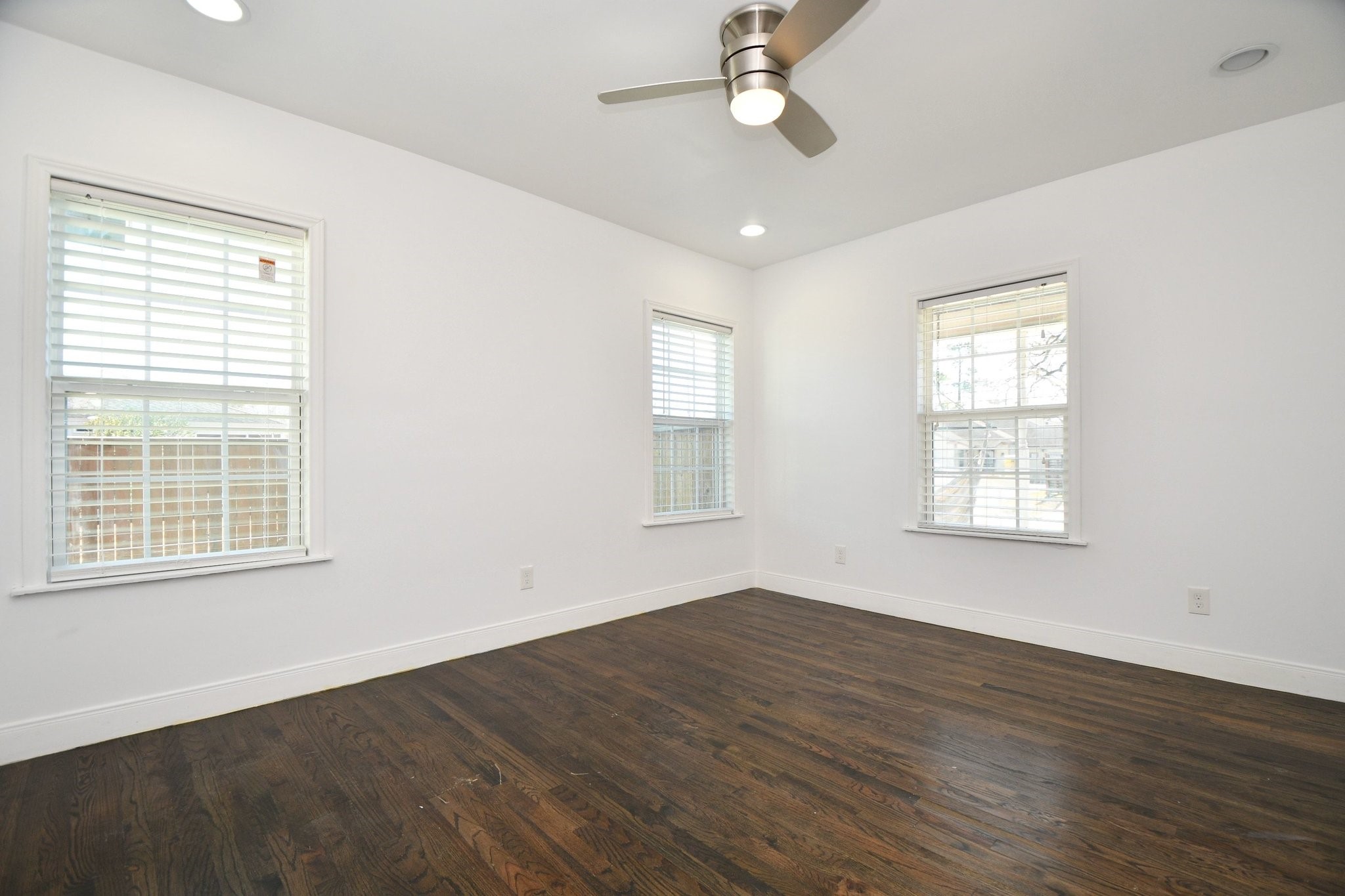 3803 Arbor Street Houston, TX 77004 - Photo 12 of 19 Bright room with dark hardwood floors, three large windows, white walls, and a ceiling fan. Perfect for a bedroom or office space.