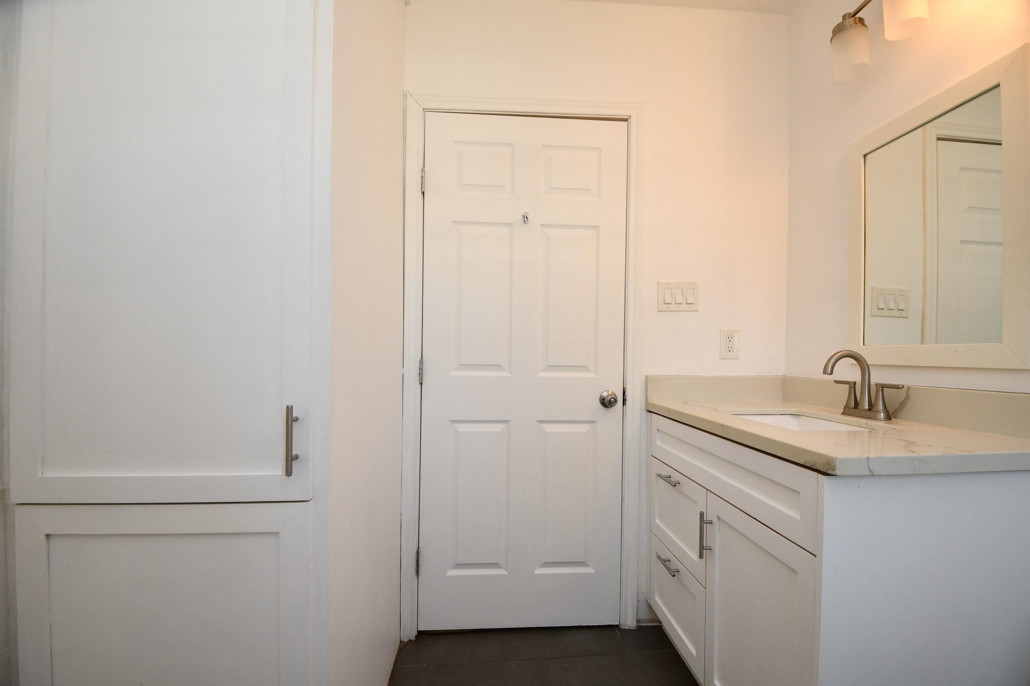 3803 Arbor Street Houston, TX 77004 - Photo 14 of 15 This bathroom features a modern vanity with a marble countertop, a sleek faucet, and ample storage. It has a clean, white finish with a large mirror and stylish light fixture, creating a bright and inviting space.