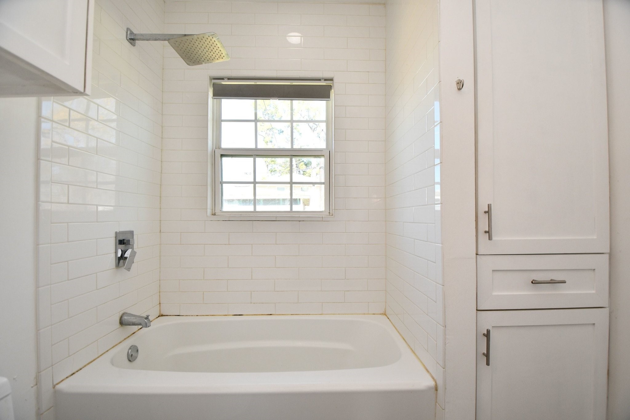 3803 Arbor Street Houston, TX 77004 - Photo 14 of 19 This bathroom features a clean, modern design with white subway tile walls, a window for natural light, and a built-in bathtub. There is also convenient storage space with a cabinet beside the tub.