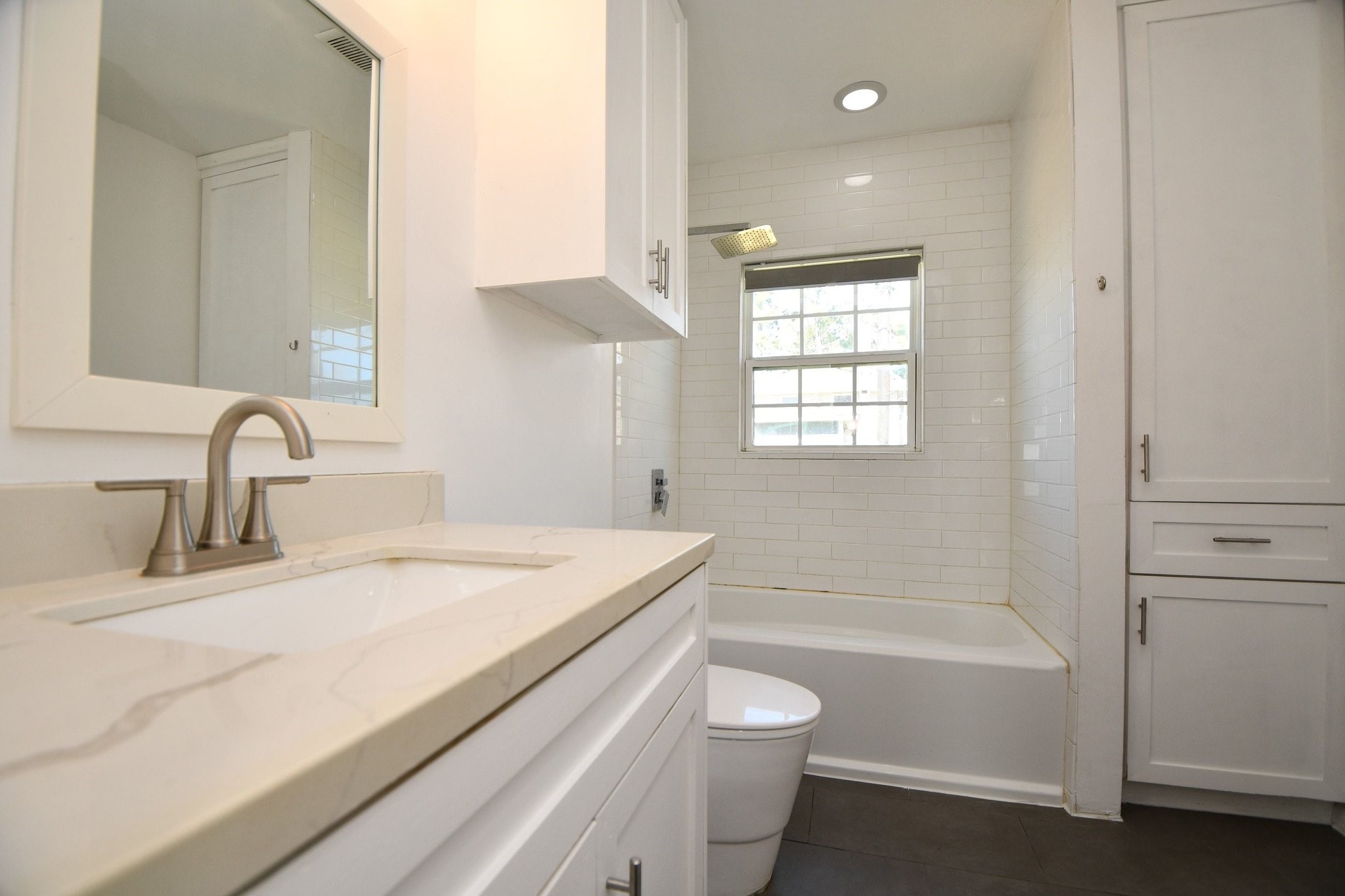 3803 Arbor Street Houston, TX 77004 - Photo 16 of 19 This bathroom features a sleek design with a white vanity and modern faucet, complemented by a subway-tiled shower and bathtub. A window provides natural light, and there’s ample cabinet storage.