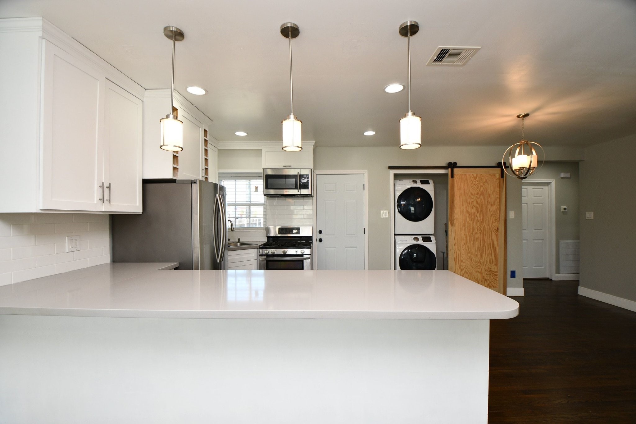 3803 Arbor Street Houston, TX 77004 - Photo 5 of 19 This modern kitchen features sleek white cabinetry, stainless steel appliances, and a spacious quartz countertop. It includes a convenient stacked washer and dryer, with stylish pendant lighting and a sliding barn door for added character.