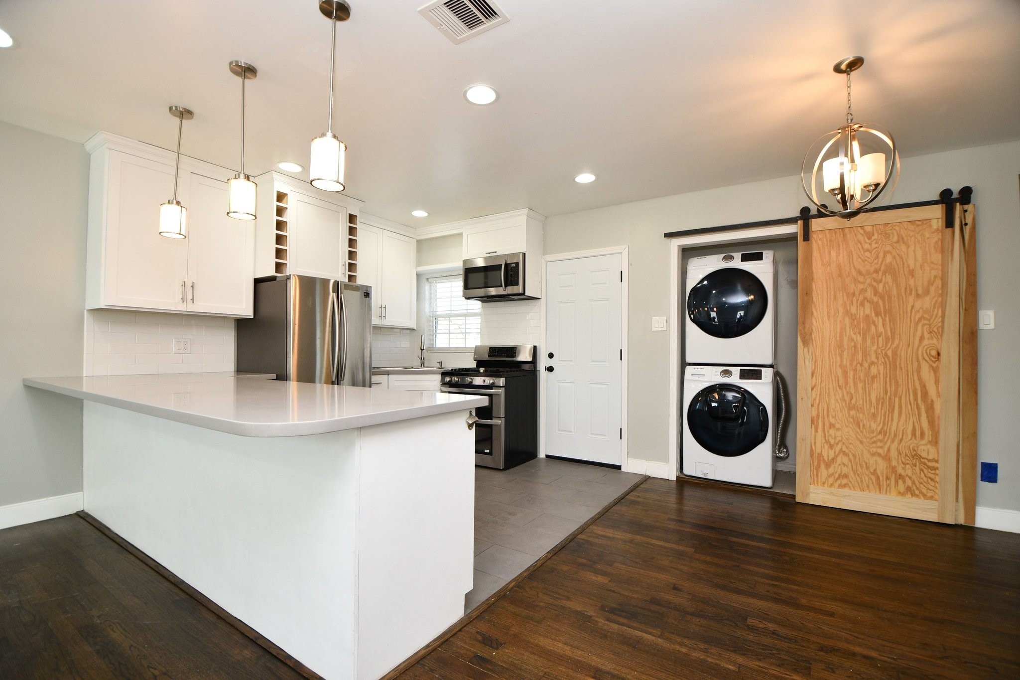 3803 Arbor Street Houston, TX 77004 - Photo 6 of 19 This photo showcases a modern kitchen with white cabinetry, stainless steel appliances, and a sleek island with pendant lighting. It features a built-in oven, gas stove, and a stylish barn door concealing a stacked washer and dryer. The space is open and well-lit, offering a clean and contemporary feel.