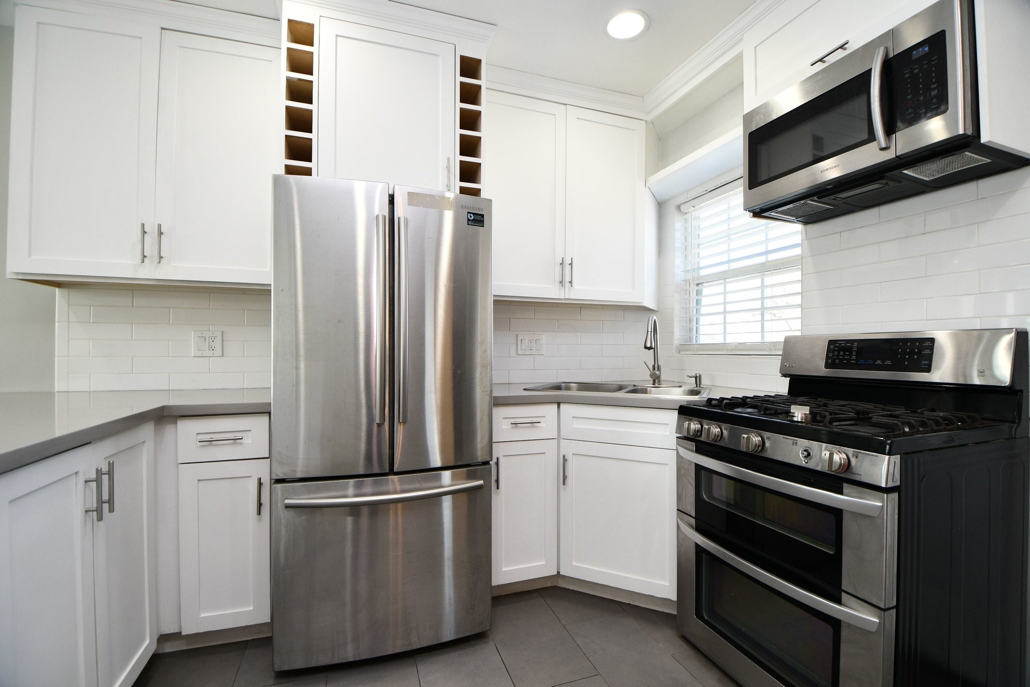 3803 Arbor Street Houston, TX 77004 - Photo 6 of 15 Modern kitchen with sleek stainless steel appliances, including a French door refrigerator and gas stove. The space features white cabinetry, subway tile backsplash, and a window for natural light.