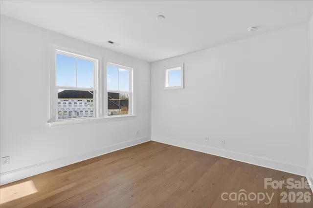 a view of an empty room with a window and hardwood floor
