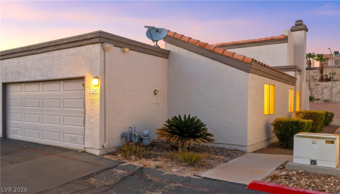 Property exterior at dusk featuring an attached garage, stucco siding, and a tile roof