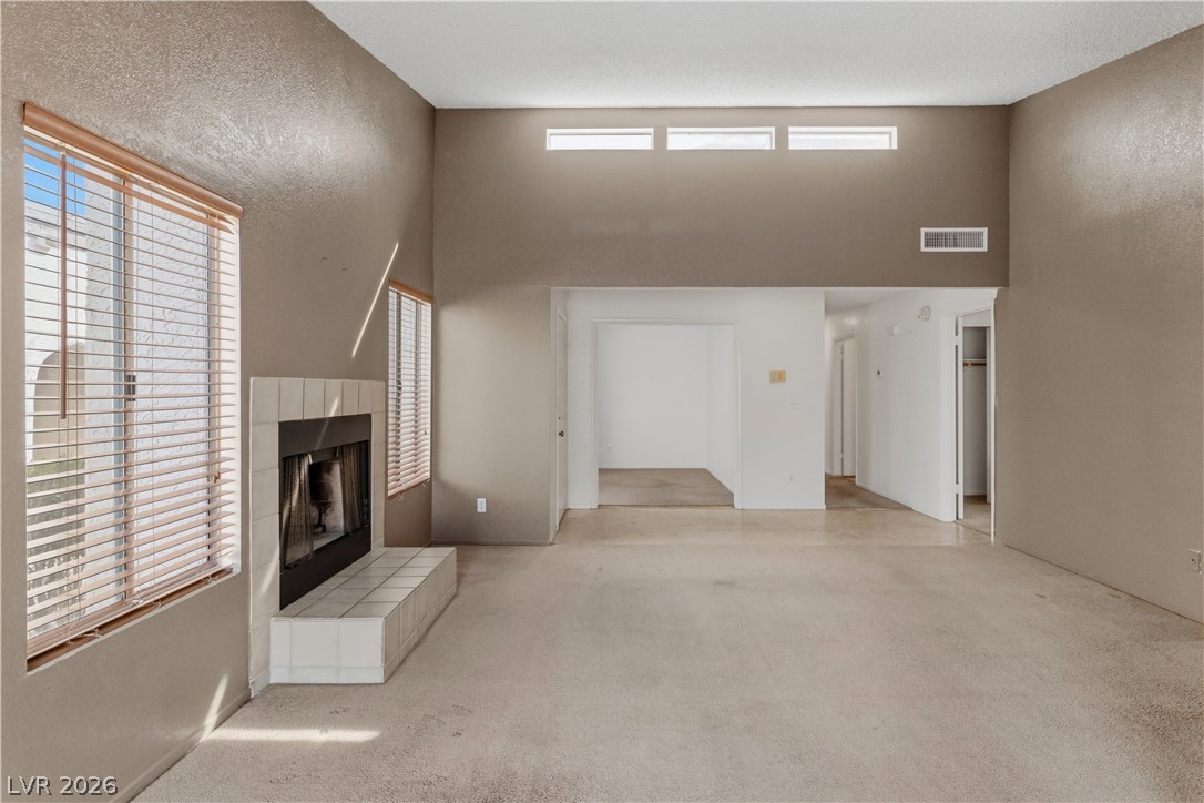 2124 Pebble Creek Lane Laughlin, NV 89029 - Photo 14 of 54 living room with a tile fireplace, light colored carpet, a high ceiling, and a textured wall