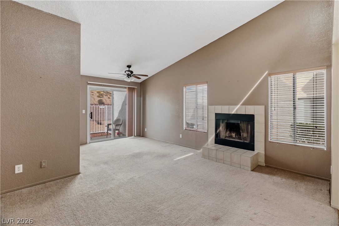 2124 Pebble Creek Lane Laughlin, NV 89029 - Photo 5 of 54 living room with a textured wall, ceiling fan, a tiled fireplace, vaulted ceiling, and light carpet