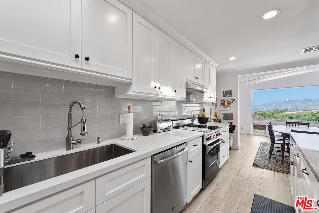 29500 Heathercliff Road, Unit 202 Malibu, CA 90265 - Photo 15 of 36 a kitchen with stainless steel appliances granite countertop a stove a sink dishwasher and white cabinets with wooden floor
