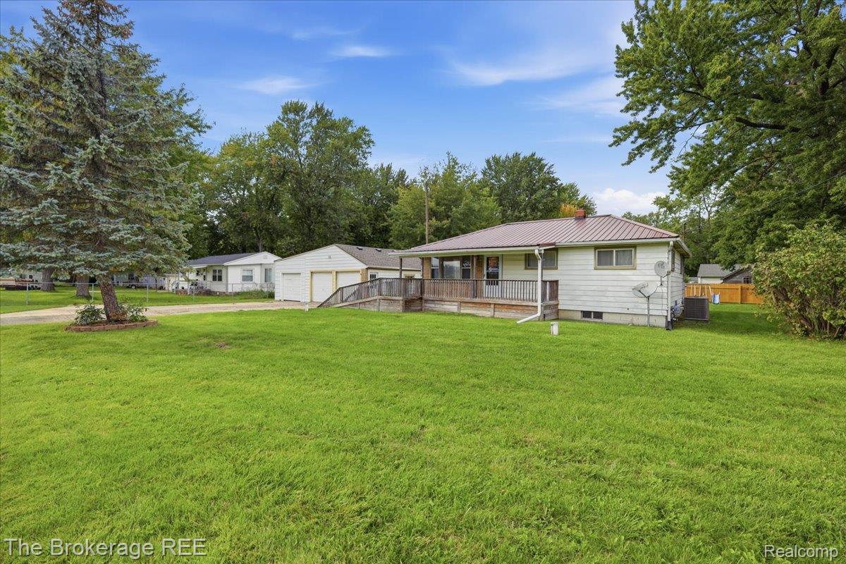 Expansive green lawn with mature trees, a detached two-car garage, a metal roof, and a wood deck with ramp access