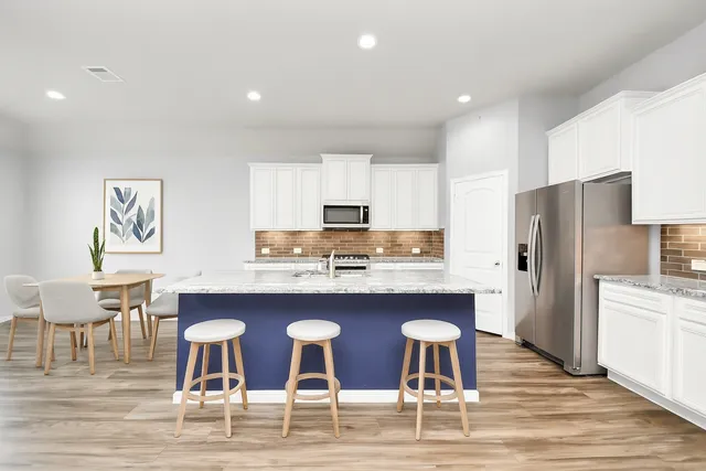 a kitchen with stainless steel appliances granite countertop a dining table chairs refrigerator and sink