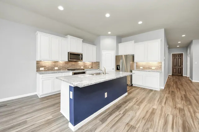 a kitchen with stainless steel appliances granite countertop a stove top oven a sink dishwasher and a refrigerator with wooden floor