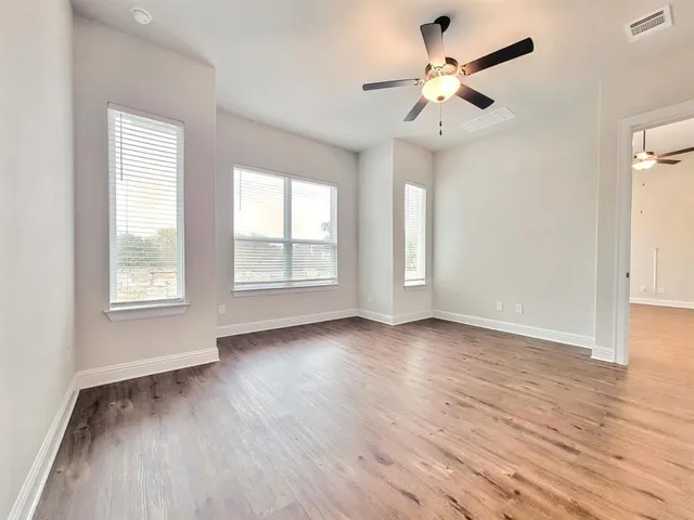 an empty room with wooden floor ceiling fan and windows