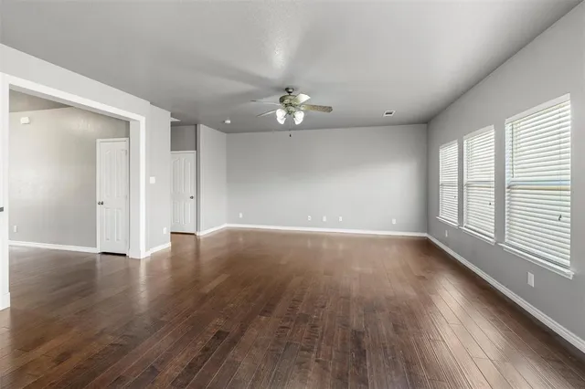 an empty room with wooden floor ceiling fan and windows