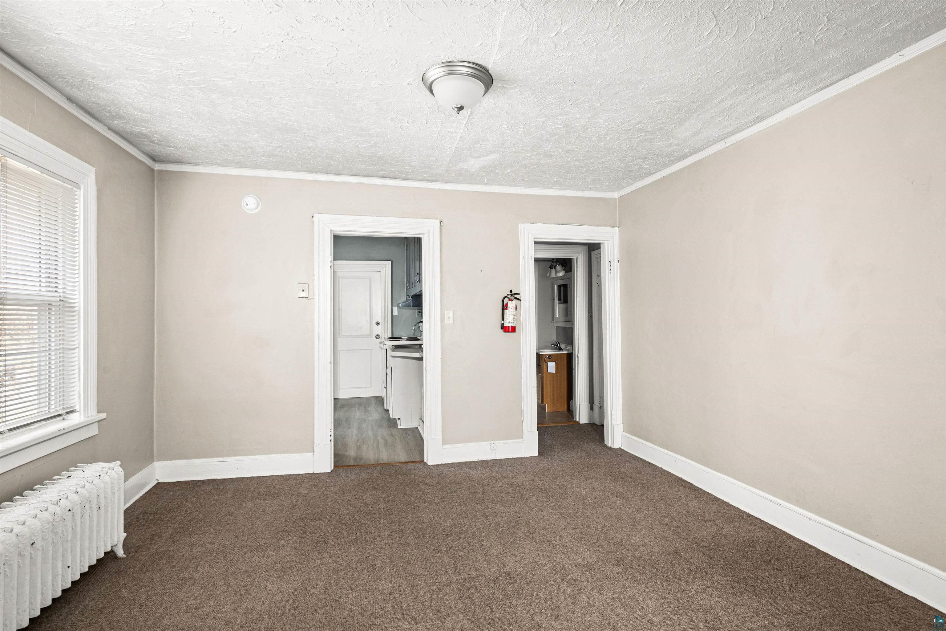 1127 East 3rd Street Duluth, MN 55805 - Photo 18 of 28 Neutral-toned room featuring a textured ceiling, a window with blinds, and a built-in radiator