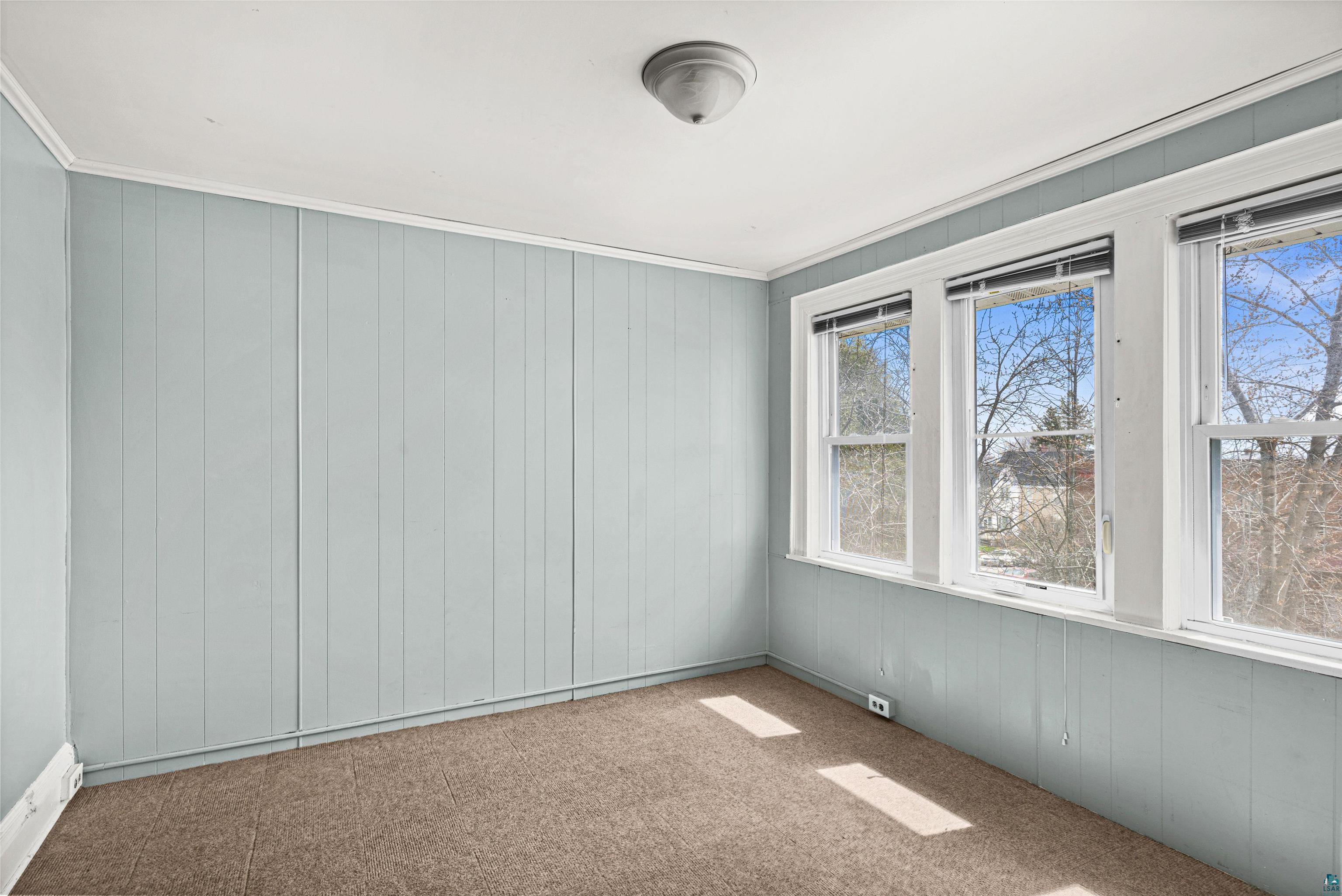 1127 East 3rd Street Duluth, MN 55805 - Photo 19 of 28 Room featuring three large windows with white trim, light blue vertical paneling, white crown molding, and a flush-mount ceiling fixture