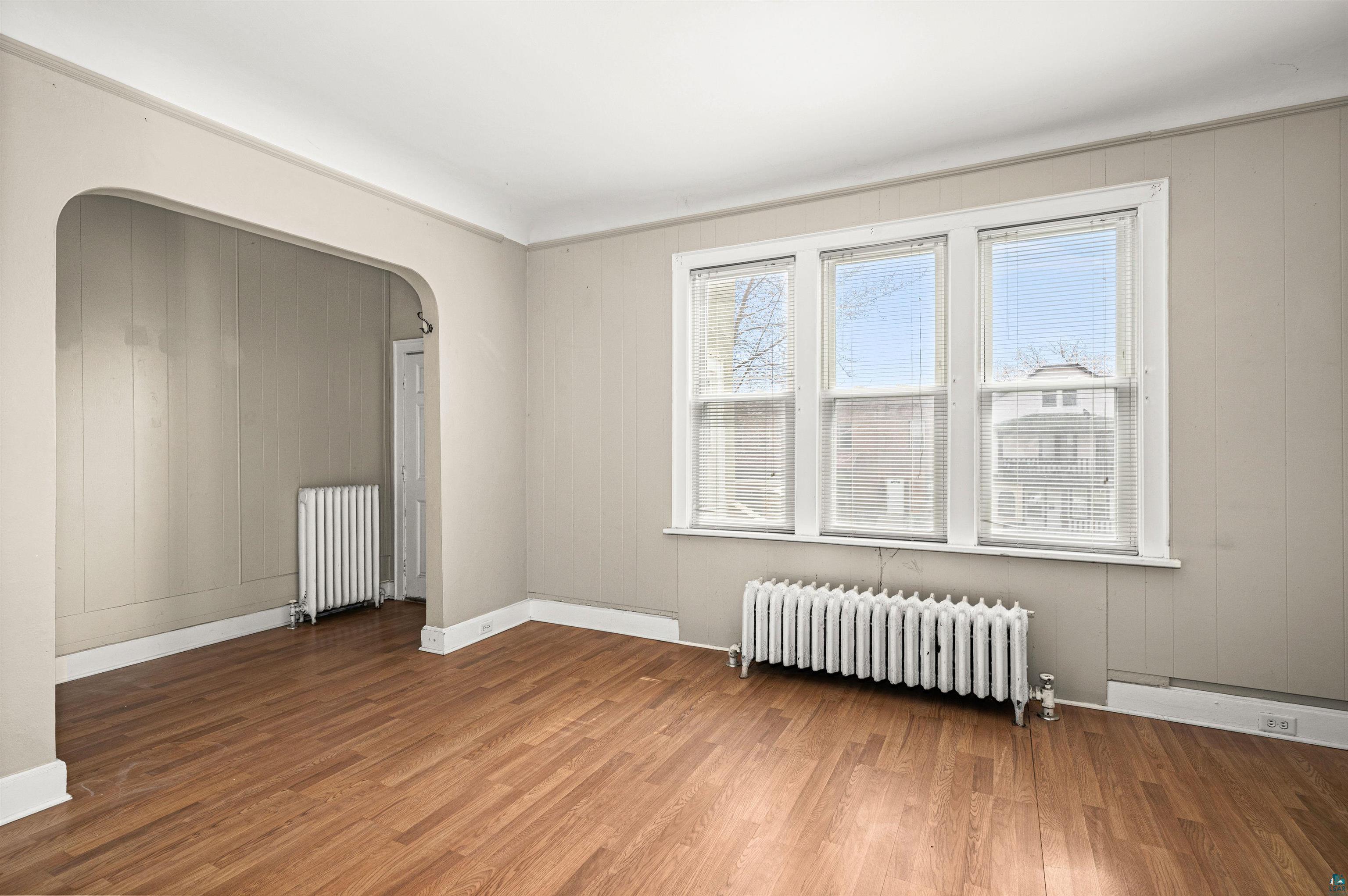 1127 East 3rd Street Duluth, MN 55805 - Photo 3 of 28 Room featuring wood-finish flooring, a trio of casement windows, two classic radiators, and an arched doorway