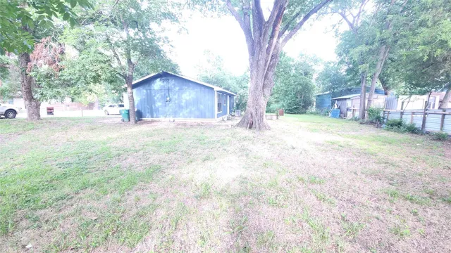 a backyard of a house with large trees and wooden fence