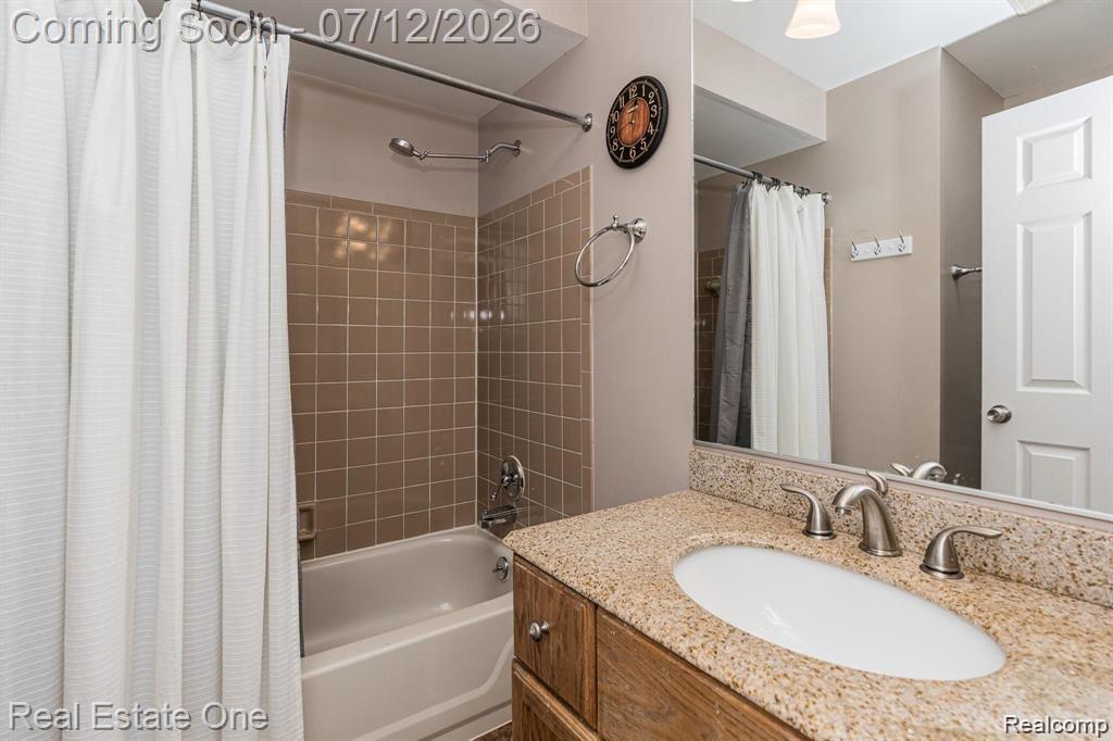 2033 Avonstoke Road Rochester, MI 48307 - Photo 13 of 26 Bathroom featuring a bathtub with tiled surround, a vanity with a granular countertop, an undermount sink, and brushed nickel fixtures