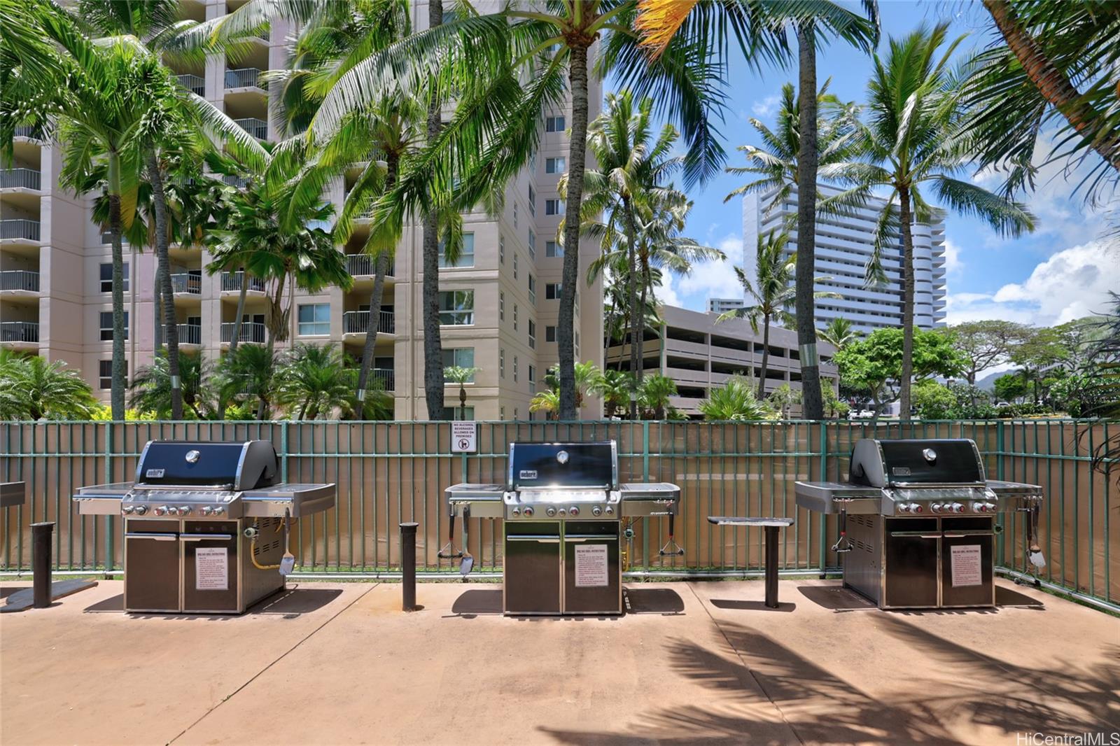3009 Ala Makahala Place, Unit 1804 Honolulu, HI 96818 - Photo 17 of 20 a patio table and chairs with potted plants and large trees