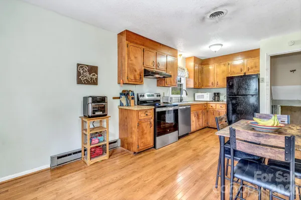 a open kitchen with stainless steel appliances a stove a refrigerator a dining table and chairs with wooden floor