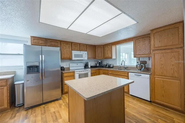 a kitchen with stainless steel appliances granite countertop a refrigerator a sink dishwasher a stove with wooden cabinets and wooden floor