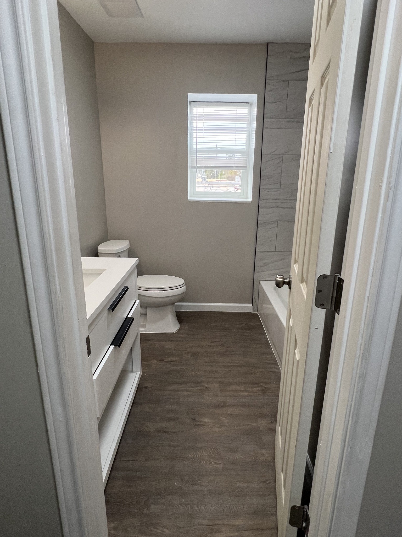 Full bathroom view from entry with updated vanity, modern mirror, and tub/shower area.