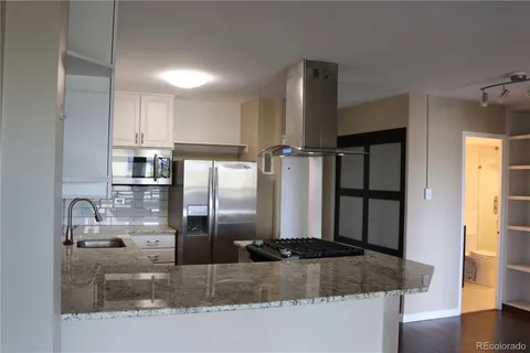 a kitchen with stainless steel appliances granite countertop a refrigerator a stove and a sink with wooden floor