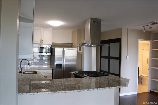 a kitchen with stainless steel appliances granite countertop a refrigerator a stove and a sink with wooden floor