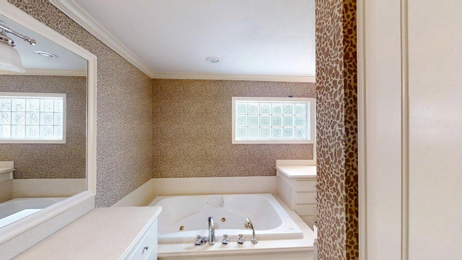 219 F Street Southwest Ardmore, OK 73401 - Photo 41 of 58 Built-in jetted tub with polished chrome fixtures, white vanity with mirror and overhead lighting, recessed lighting, and a glass block window